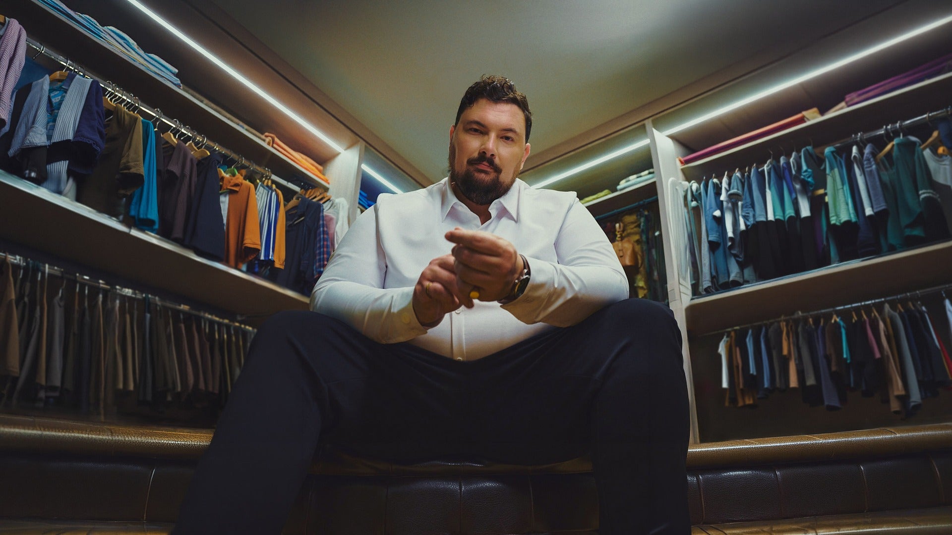 Man wearing a white dress shirt, seated in a walk-in closet